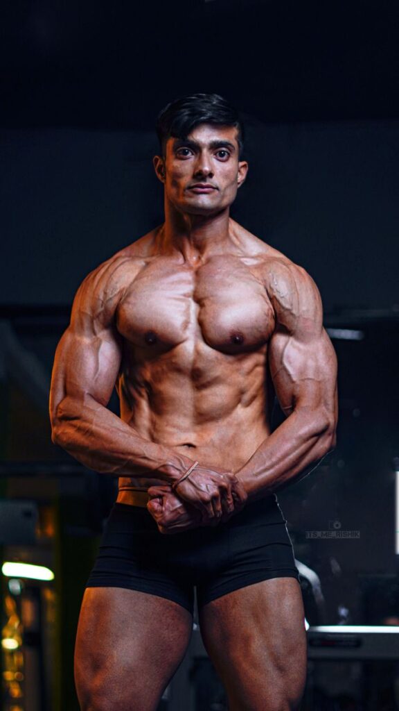 pexels photobody transformation 11805574 A brawny South Asian bodybuilder flexing muscles in a gym, showcasing strength and masculinity.