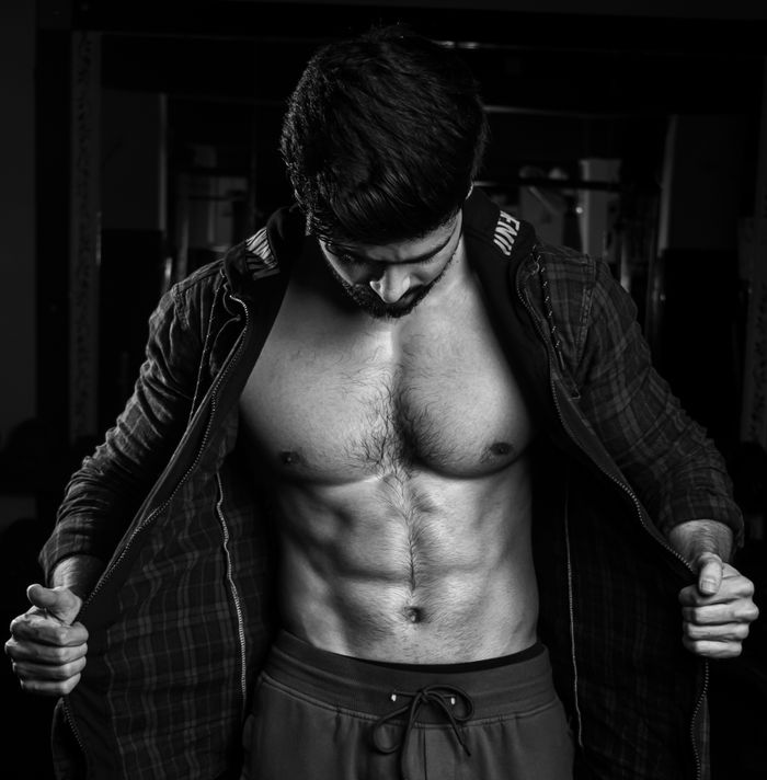 Black and white portrait of a muscular man flexing in a gym setting, showcasing physique.